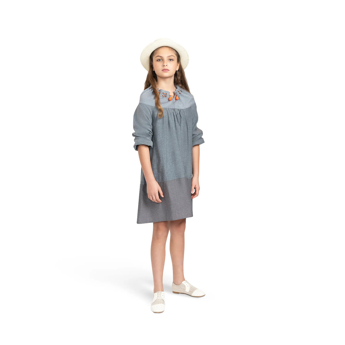 Girl modeling Puvu Pior® dark chambray dress, styled with straw hat, showing rolled sleeves and gathered neck.