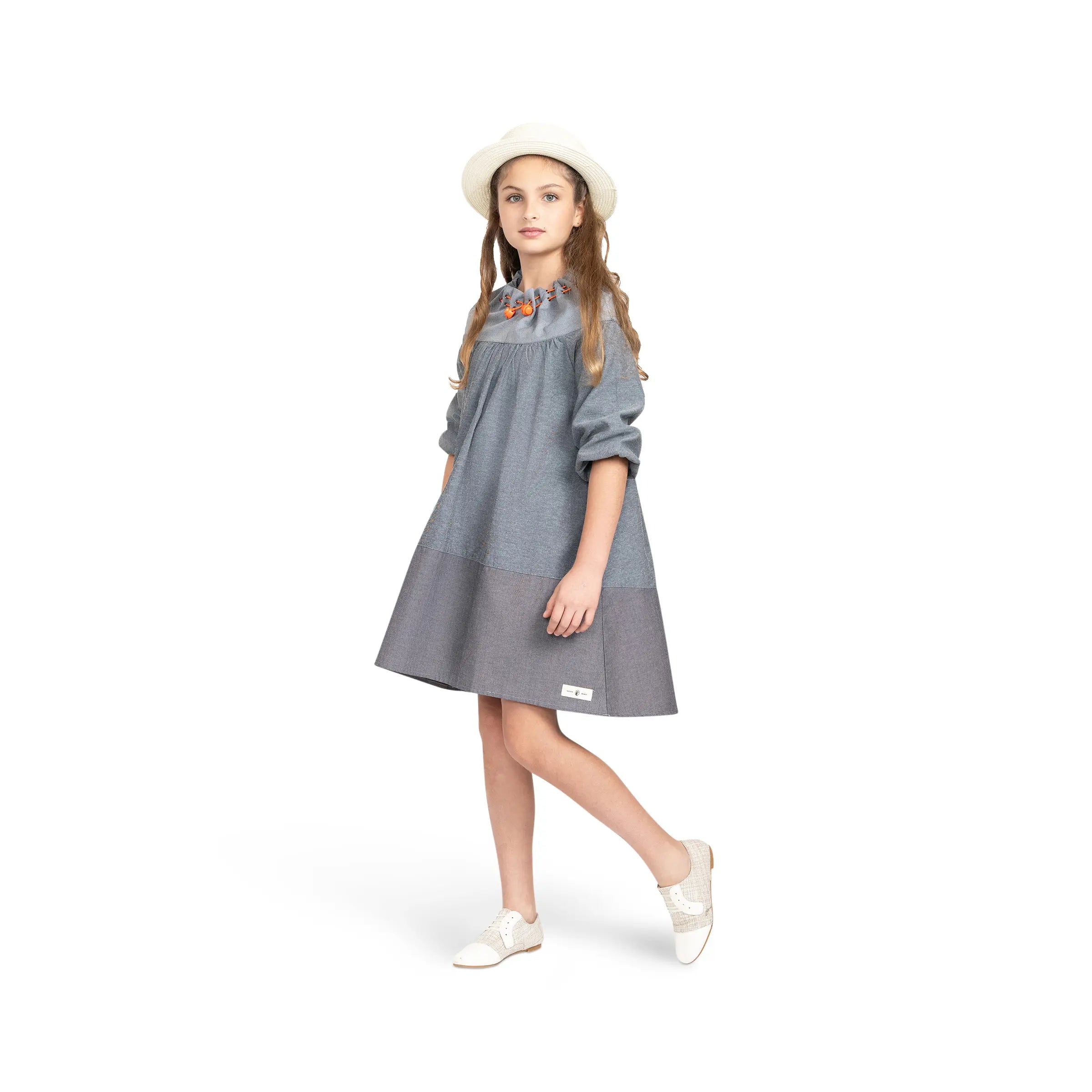 Girl in Puvu Pior® colorblock chambray dress, posed to show the movement of the flared A-line skirt and roll-up sleeves.