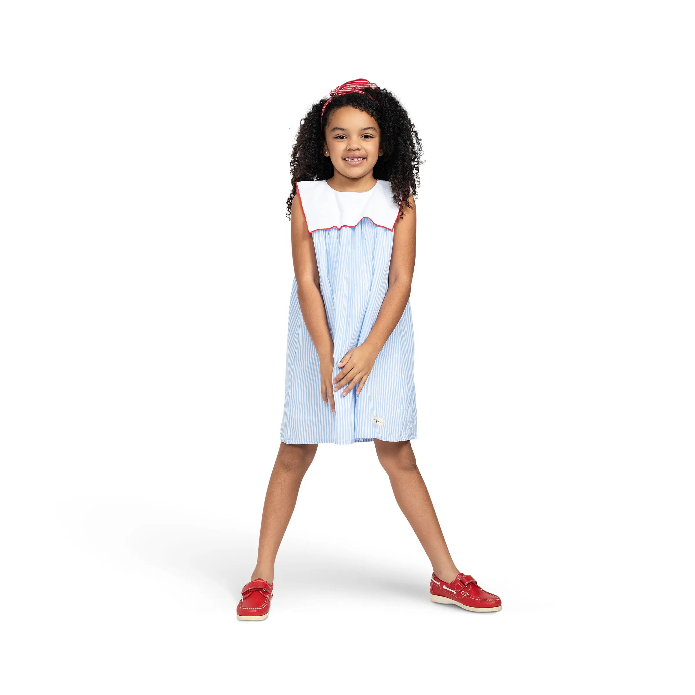 Girl modeling Puvu Pior® blue striped dress with sailor collar, styled with red headband and matching shoes.