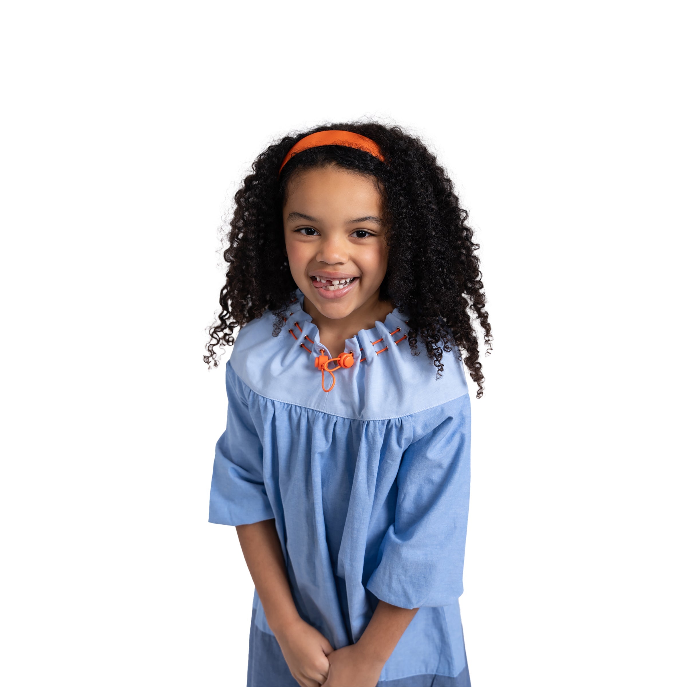 Smiling girl close-up in Puvu Pior® light chambray dress, highlighting the orange headband and drawstring collar toggles.