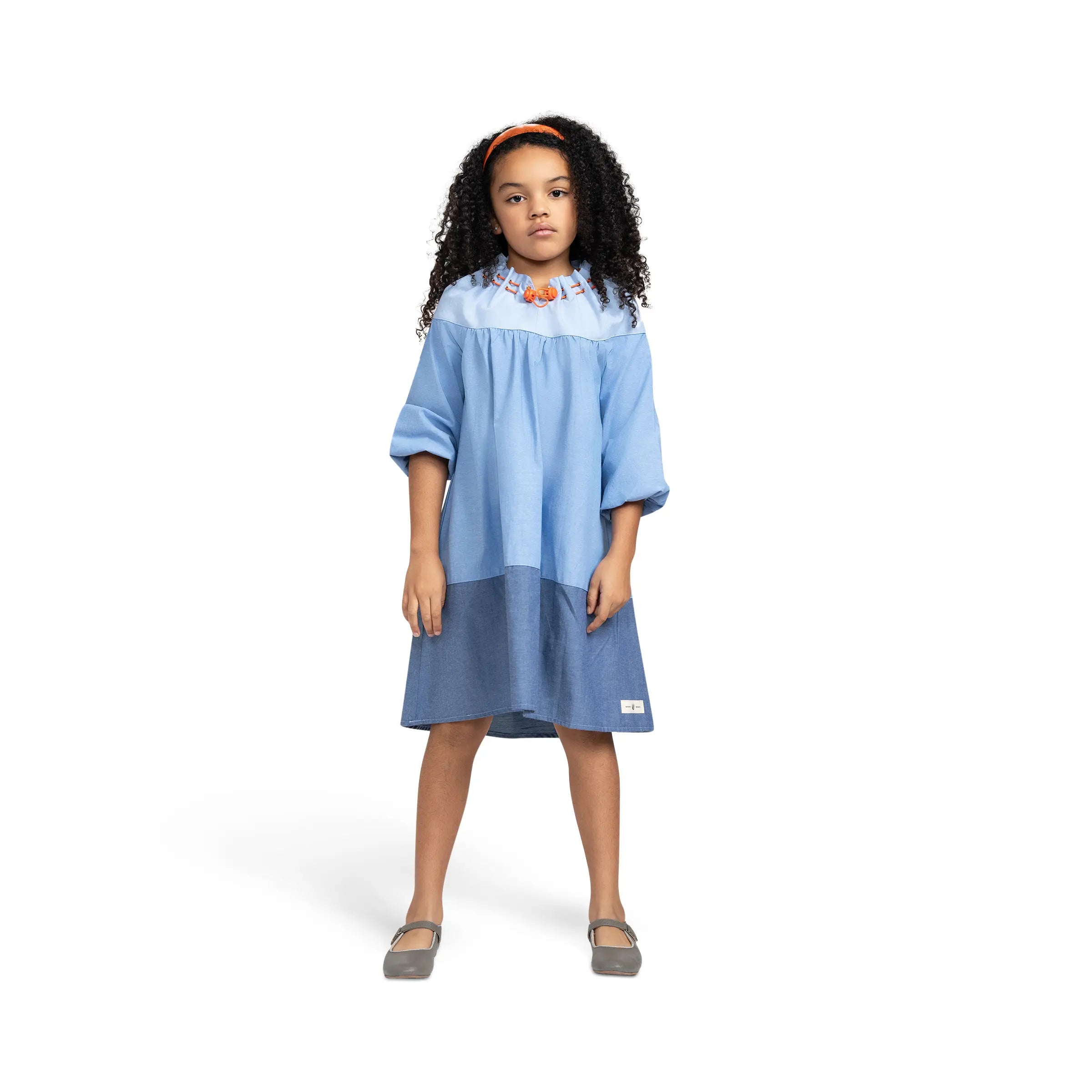 Girl modeling Puvu Pior® light blue chambray dress with orange headband, showing fit and gathered neck details.